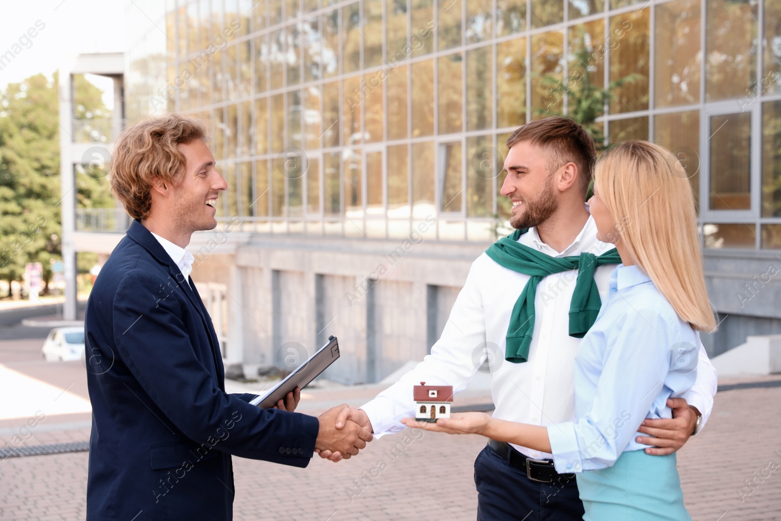 Photo of Male real estate agent shaking hands with clients outdoors