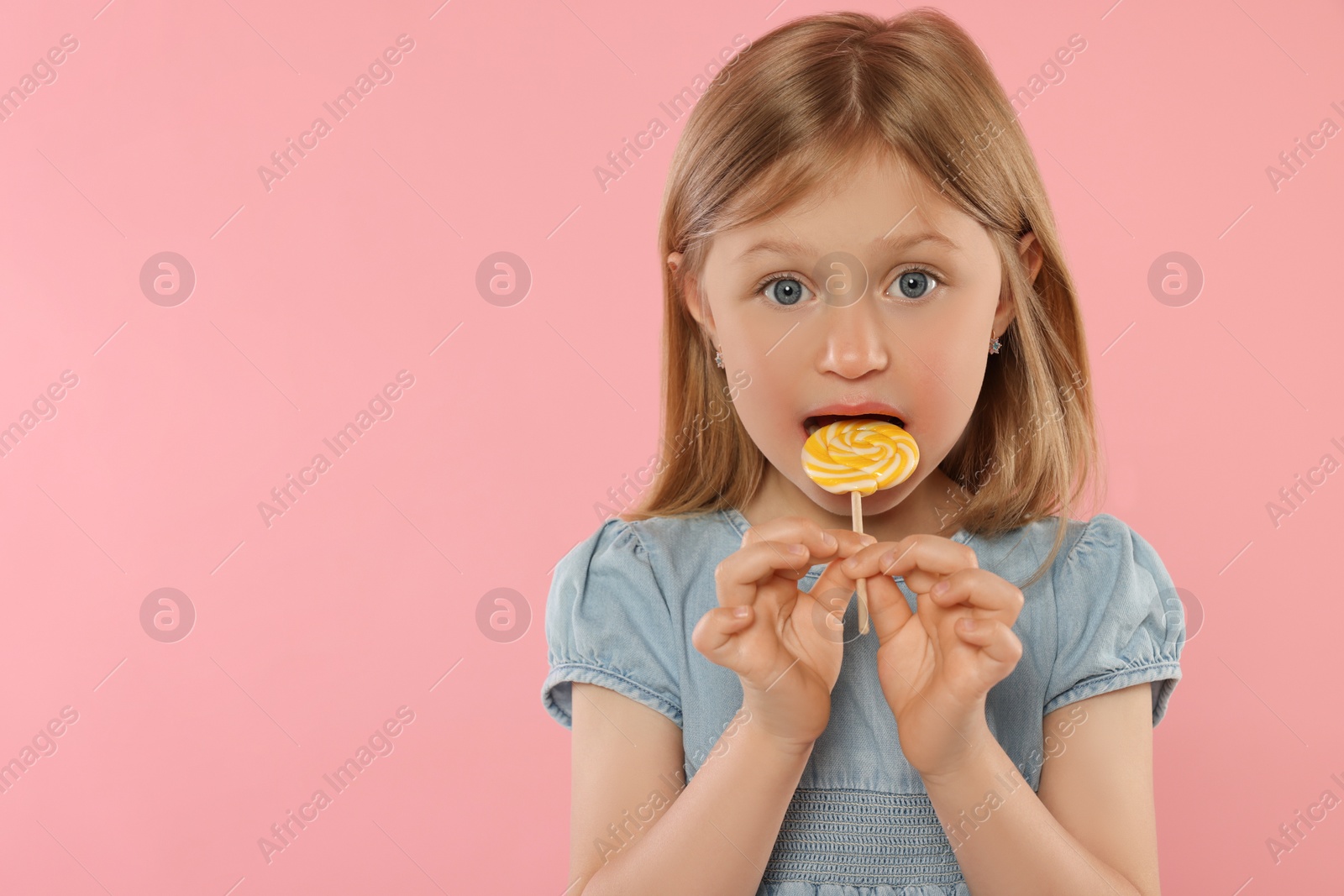 Photo of Portrait of cute girl licking lollipop on pink background, space for text