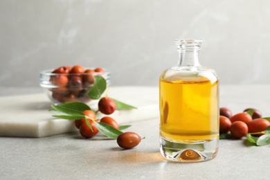 Jojoba oil in glass bottle and seeds on light grey table