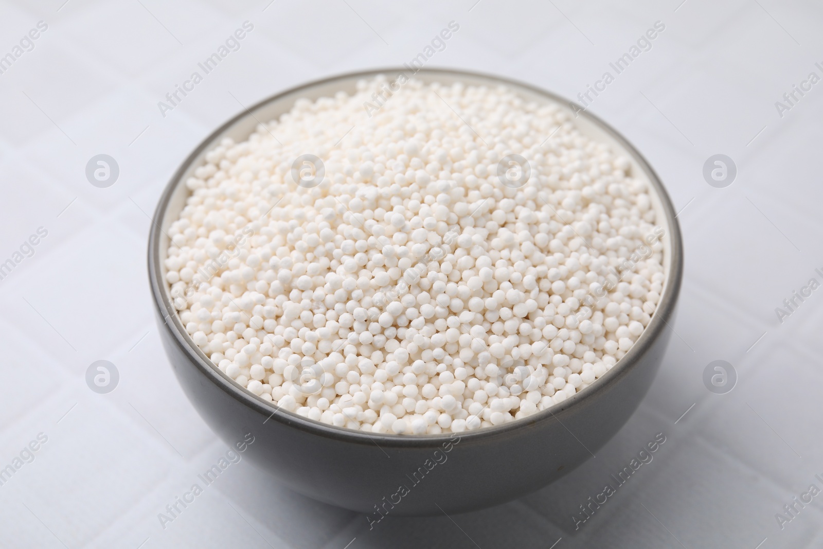 Photo of Tapioca pearls in bowl on white tiled table, closeup