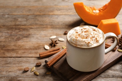 Cup with tasty pumpkin spice latte and space for text on wooden table