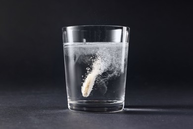 Photo of Effervescent pill dissolving in glass of water on grey table