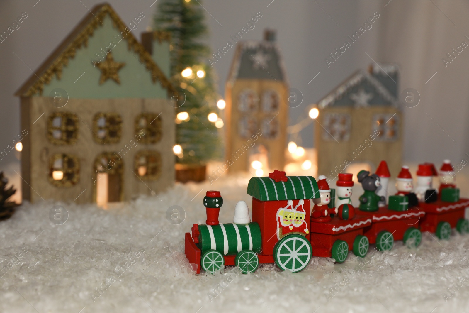 Photo of Bright toy train near decorative houses with Christmas lights on artificial snow