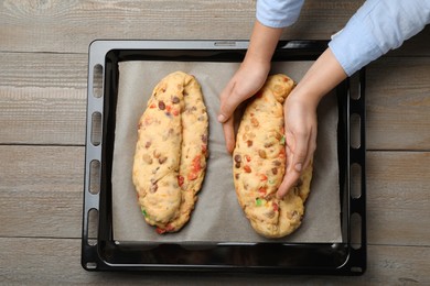 Photo of Woman making Stollen with candied fruits and nuts on baking tray at wooden table, top view. Baking traditional German Christmas bread