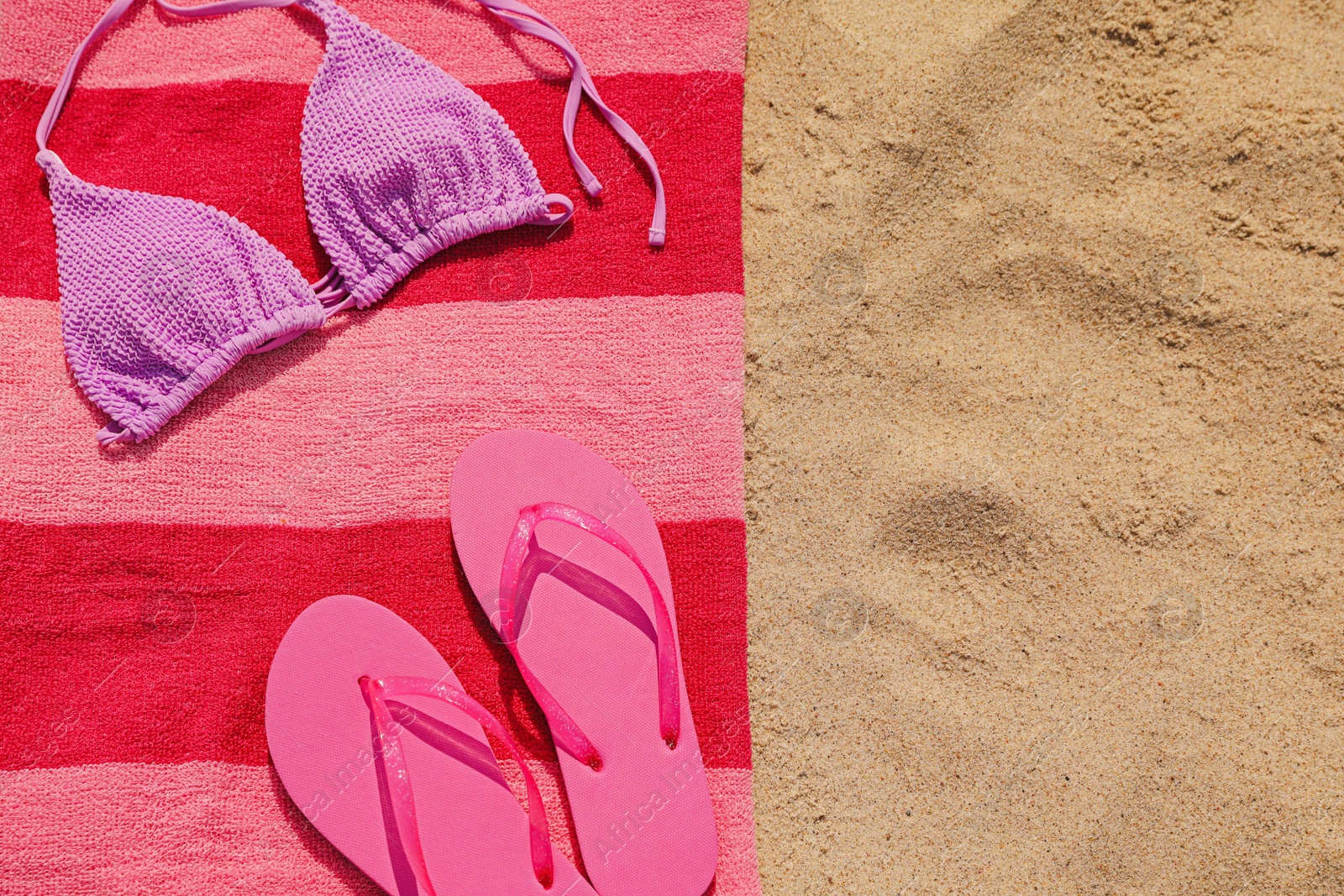 Photo of Beach towel with slippers and swimsuit on sand, top view. Space for text