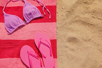 Beach towel with slippers and swimsuit on sand, top view. Space for text