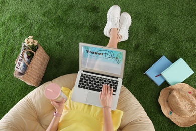 Woman and laptop with travel blogger site on artificial grass, top view