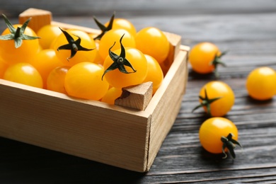 Photo of Ripe yellow tomatoes in crate on dark wooden table