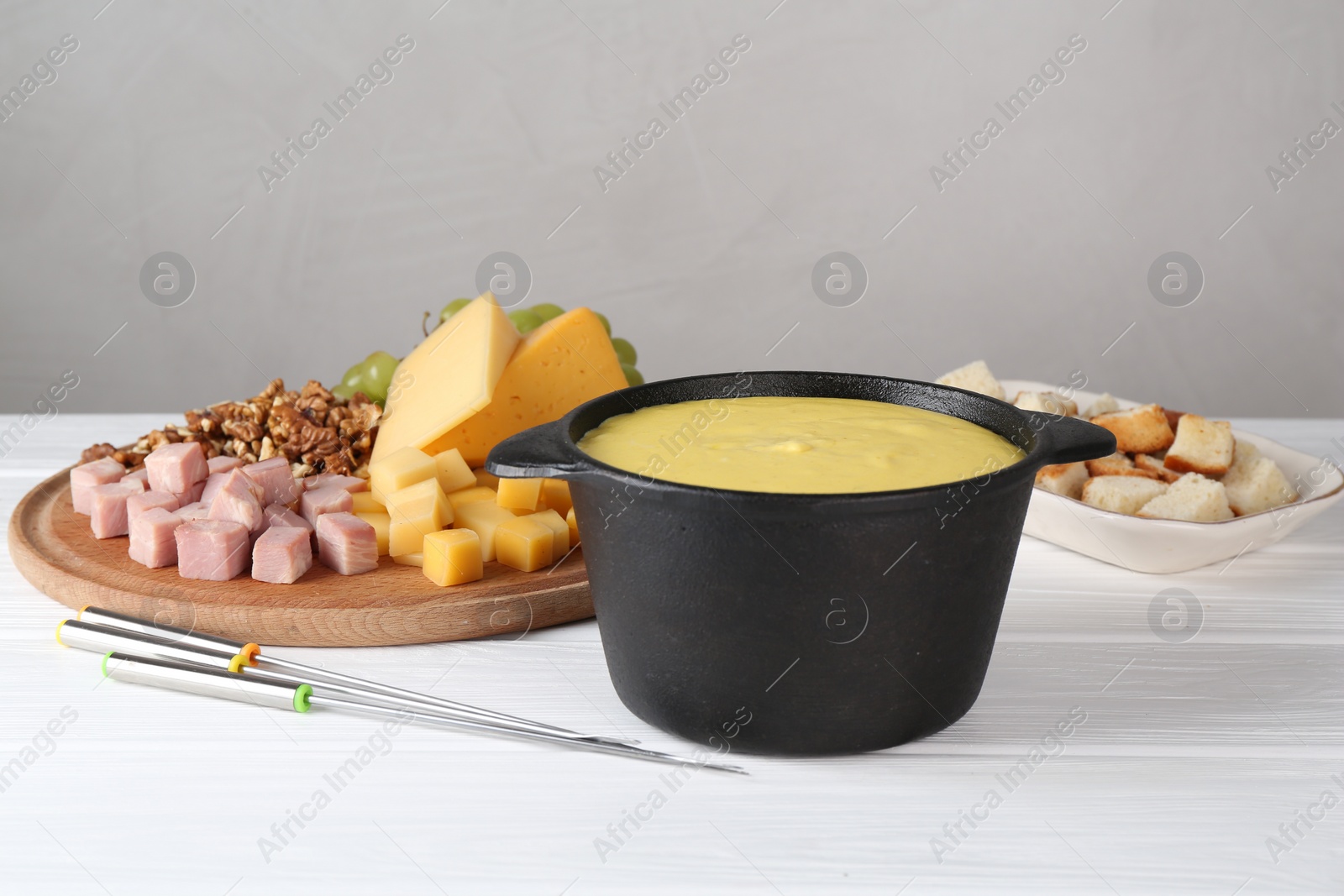 Photo of Fondue with tasty melted cheese, forks and different products on white wooden table