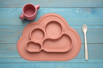 Set of plastic dishware on light blue wooden background, flat lay. Serving baby food