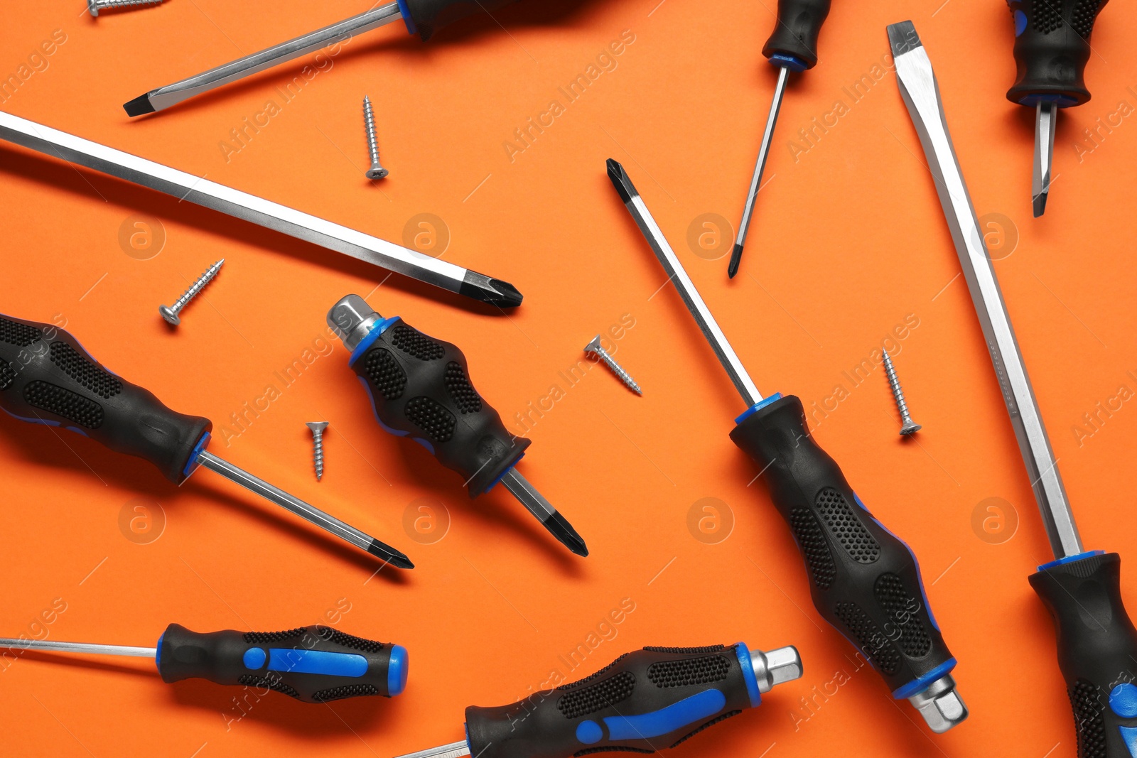 Photo of Set of screwdrivers and screws on orange background, flat lay