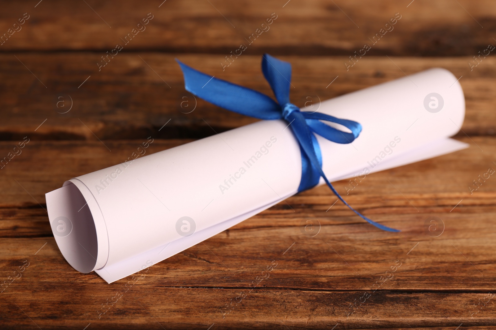 Photo of Rolled student's diploma with blue ribbon on wooden table