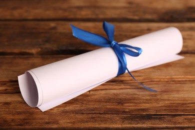 Photo of Rolled student's diploma with blue ribbon on wooden table