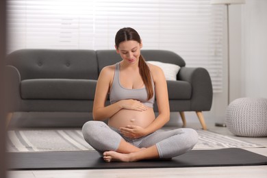 Photo of Pregnant woman sitting on yoga mat at home