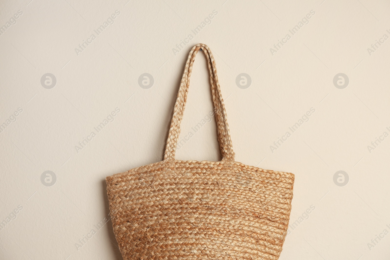 Photo of Elegant woman's straw bag hanging on beige background