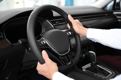 Prospective buyer holding hands on automobile steering wheel. Test drive