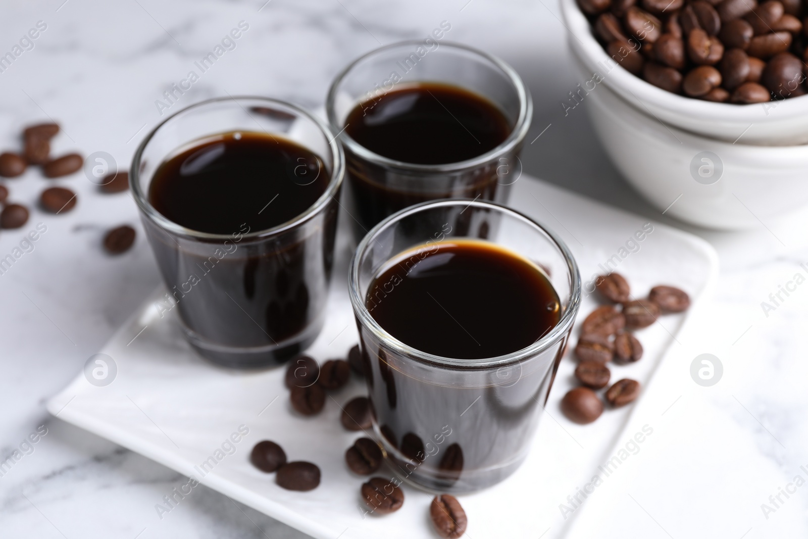 Photo of Glasses of coffee liqueur and beans on white marble table, closeup