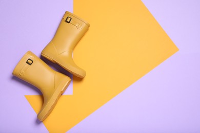 Photo of Pair of yellow rubber boots on color background, top view. Space for text