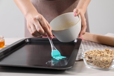 Photo of Making delicious baklava. Woman buttering baking pan at white table, closeup