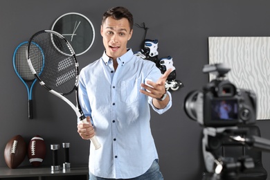 Photo of Sport blogger with tennis racket recording video on camera indoors