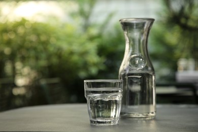 Photo of Jug and glass of fresh water on grey table outdoors. Space for text