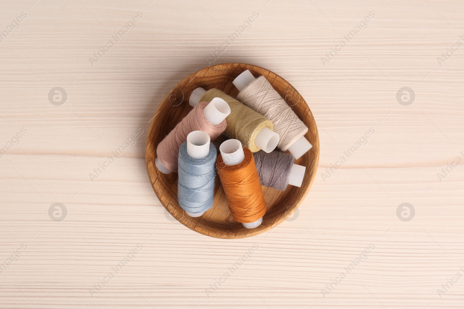 Photo of Bowl with color sewing threads on wooden table, top view