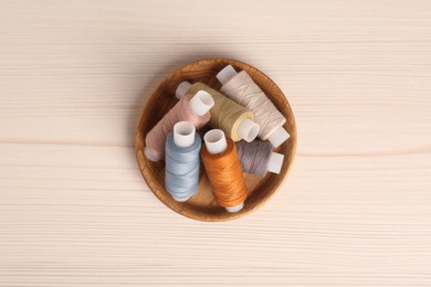 Photo of Bowl with color sewing threads on wooden table, top view