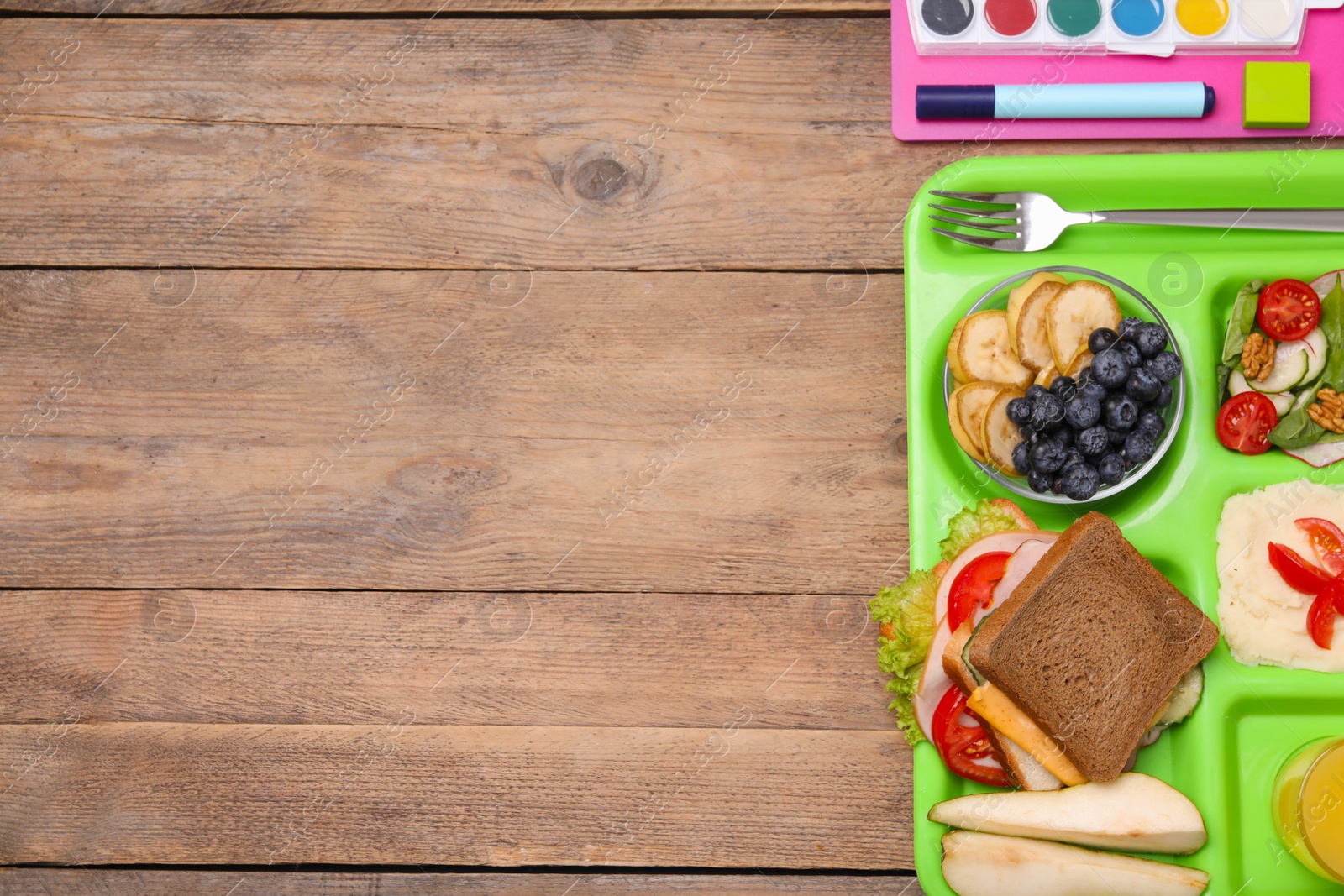Photo of Flat lay composition with serving tray of tasty healthy food and school stationery on wooden table. Space for text