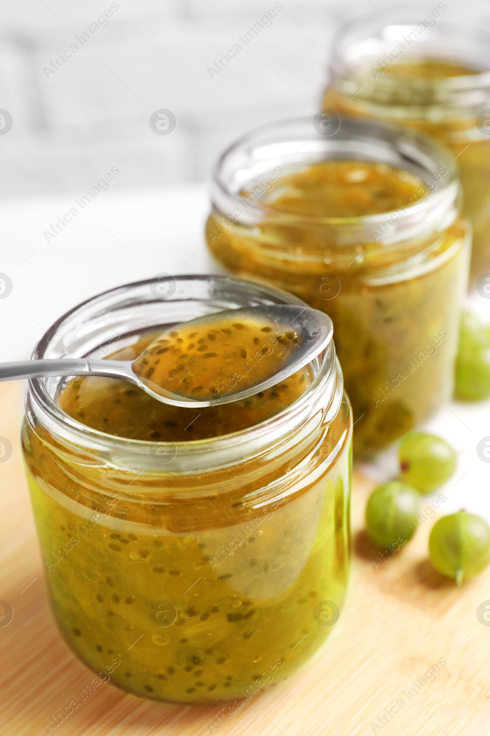 Photo of Jars of delicious gooseberry jam and fresh berries on table, closeup