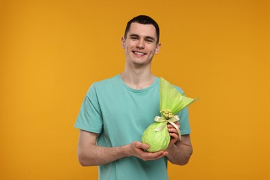 Photo of Easter celebration. Handsome young man with wrapped gift on orange background