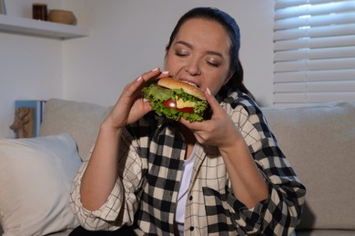 Photo of Overweight woman eating burger on sofa at home