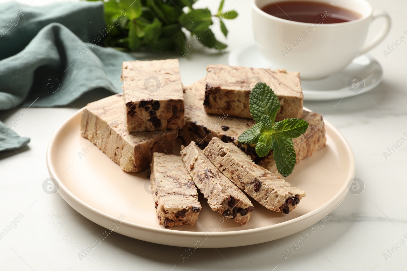 Photo of Pieces of tasty chocolate halva and mint served on white marble table, closeup