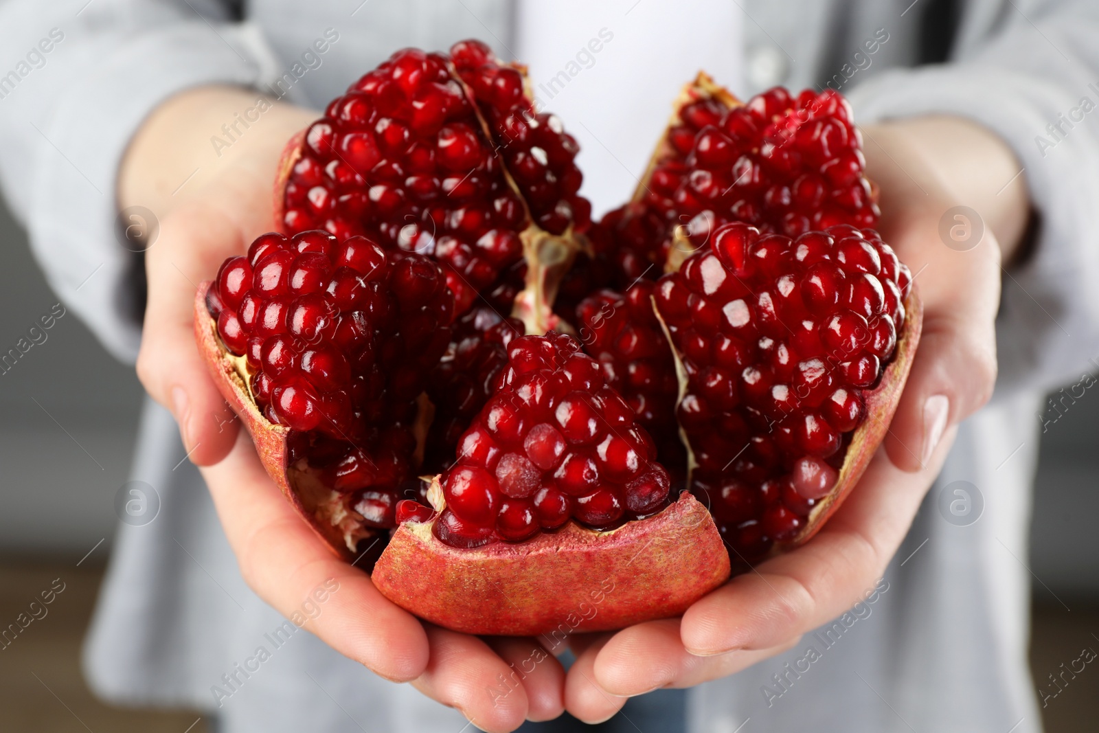 Photo of Woman holding fresh pomegranate on grey background, closeup