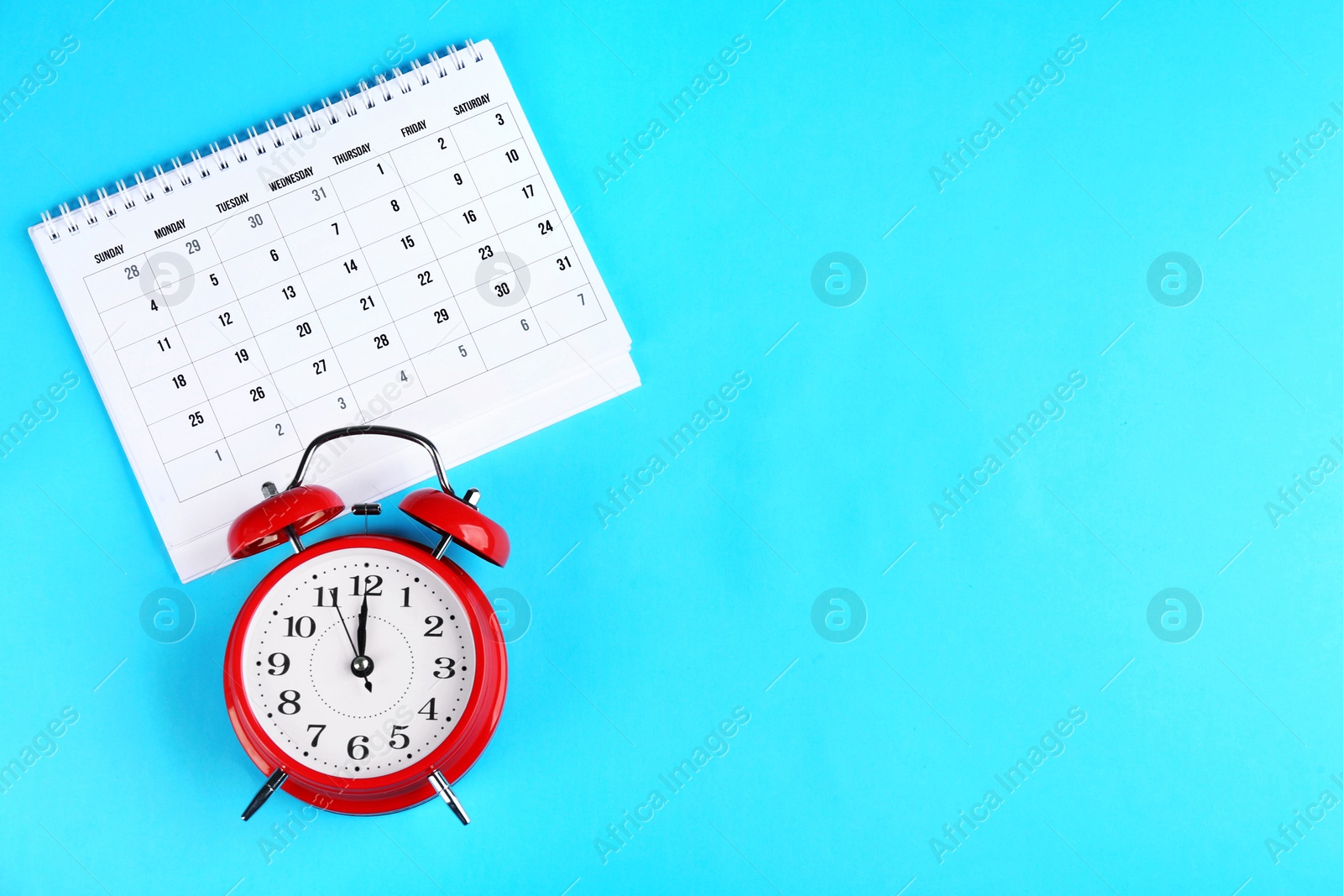 Photo of Calendar and alarm clock on light blue background, flat lay. Space for text