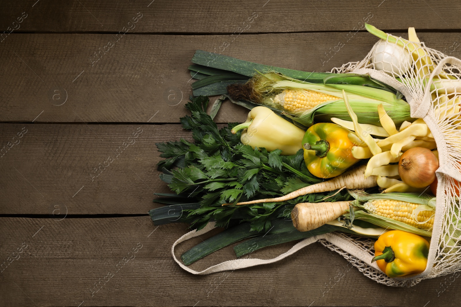 Photo of Different fresh ripe vegetables in net bag on wooden table, top view. Space for text