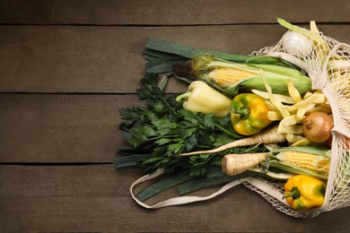 Photo of Different fresh ripe vegetables in net bag on wooden table, top view. Space for text