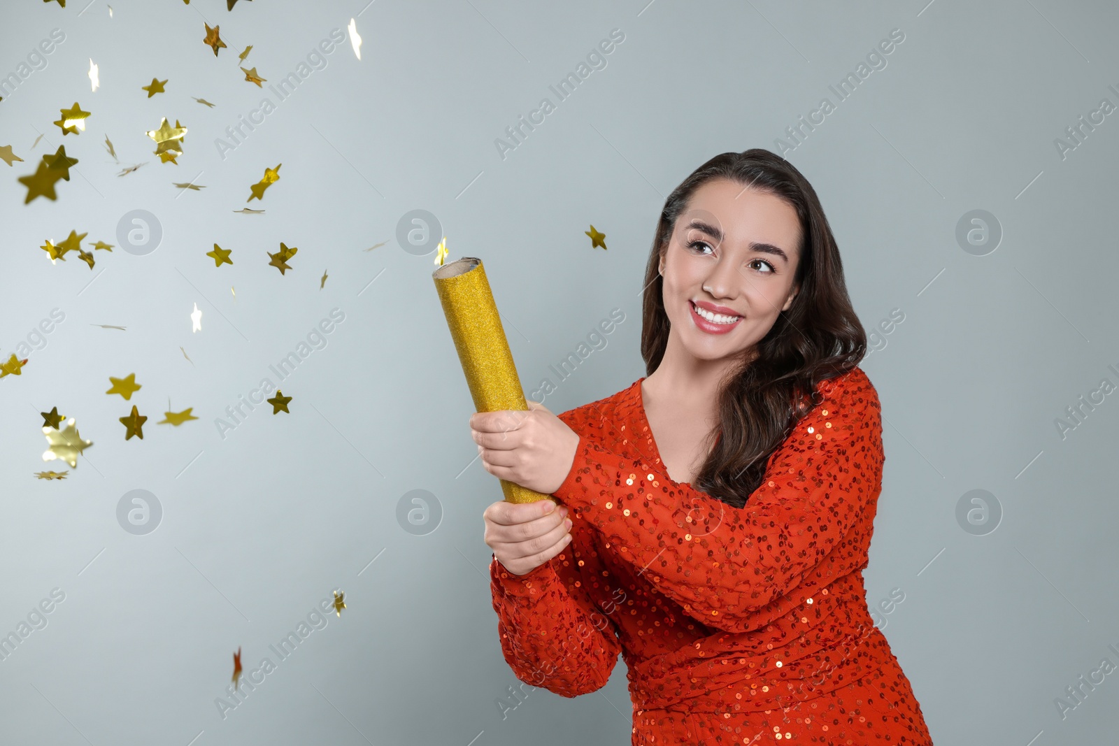 Photo of Young woman blowing up party popper on light grey background