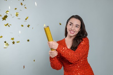 Photo of Young woman blowing up party popper on light grey background