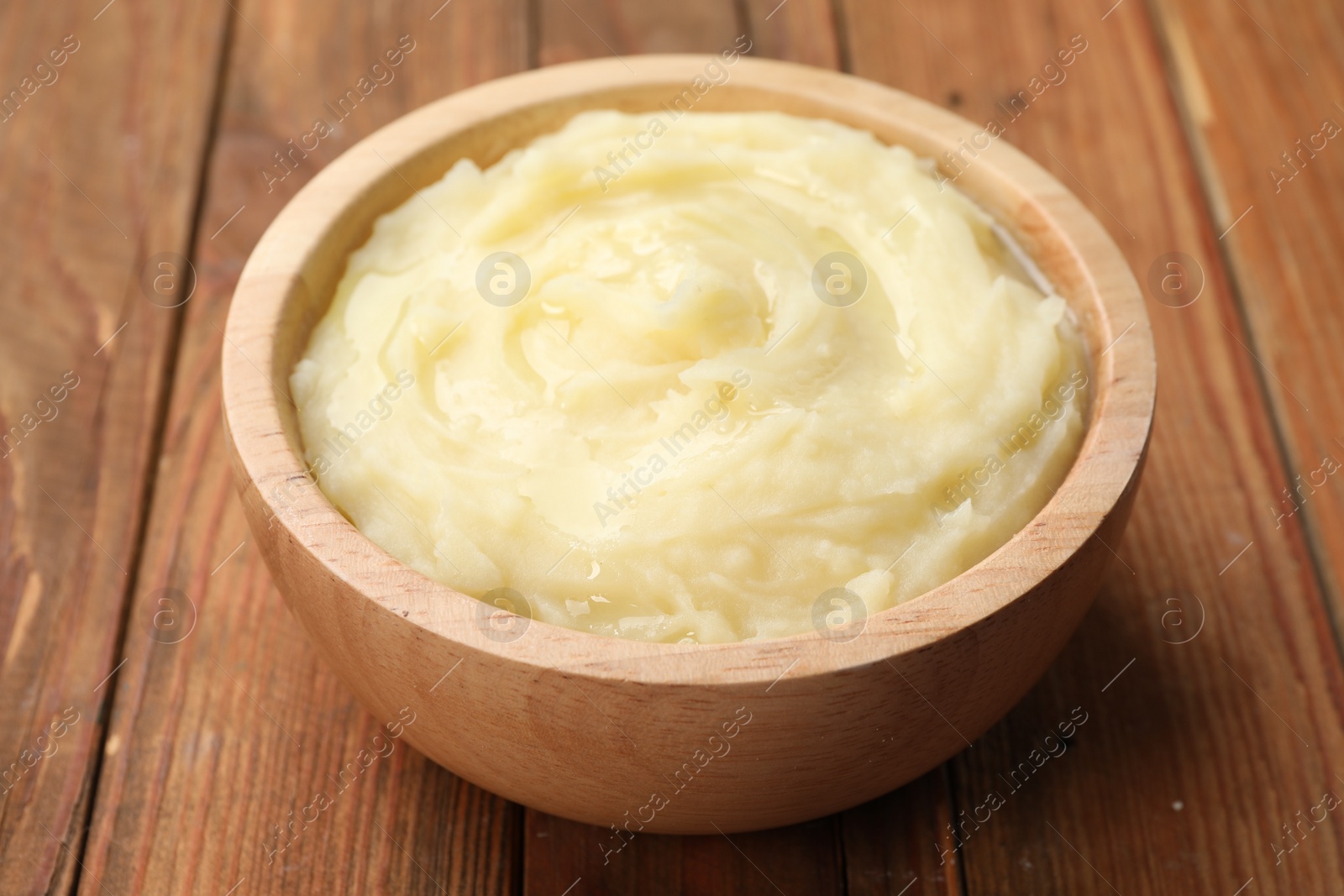 Photo of Bowl of tasty mashed potato on wooden table, closeup