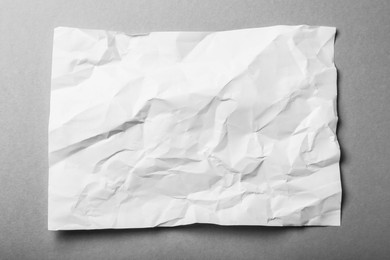 Sheet of white crumpled paper on grey background, top view