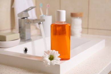 Fresh mouthwash in bottle and chamomile on sink in bathroom, closeup
