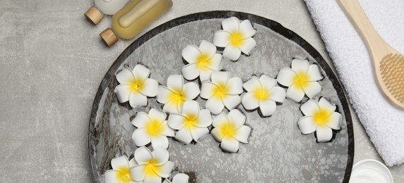 Bowl of water with flowers and different spa supplies on light grey table, flat lay