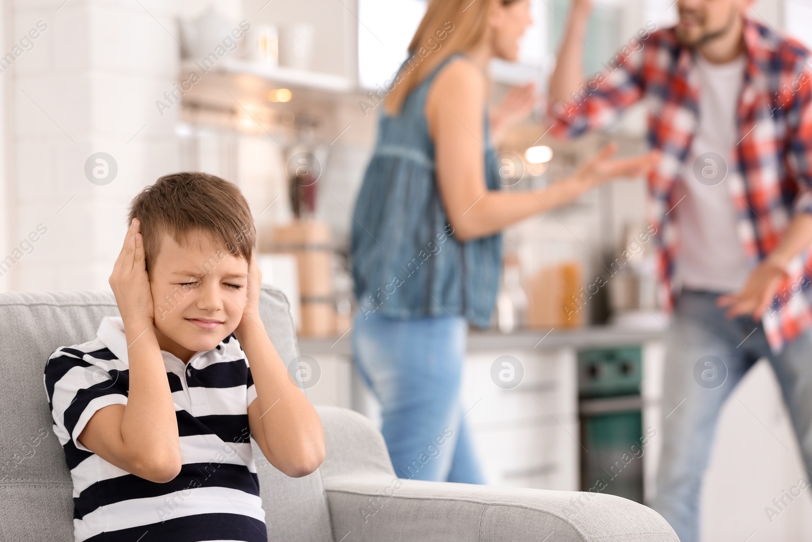 Photo of Little unhappy boy sitting on sofa while parents arguing at home