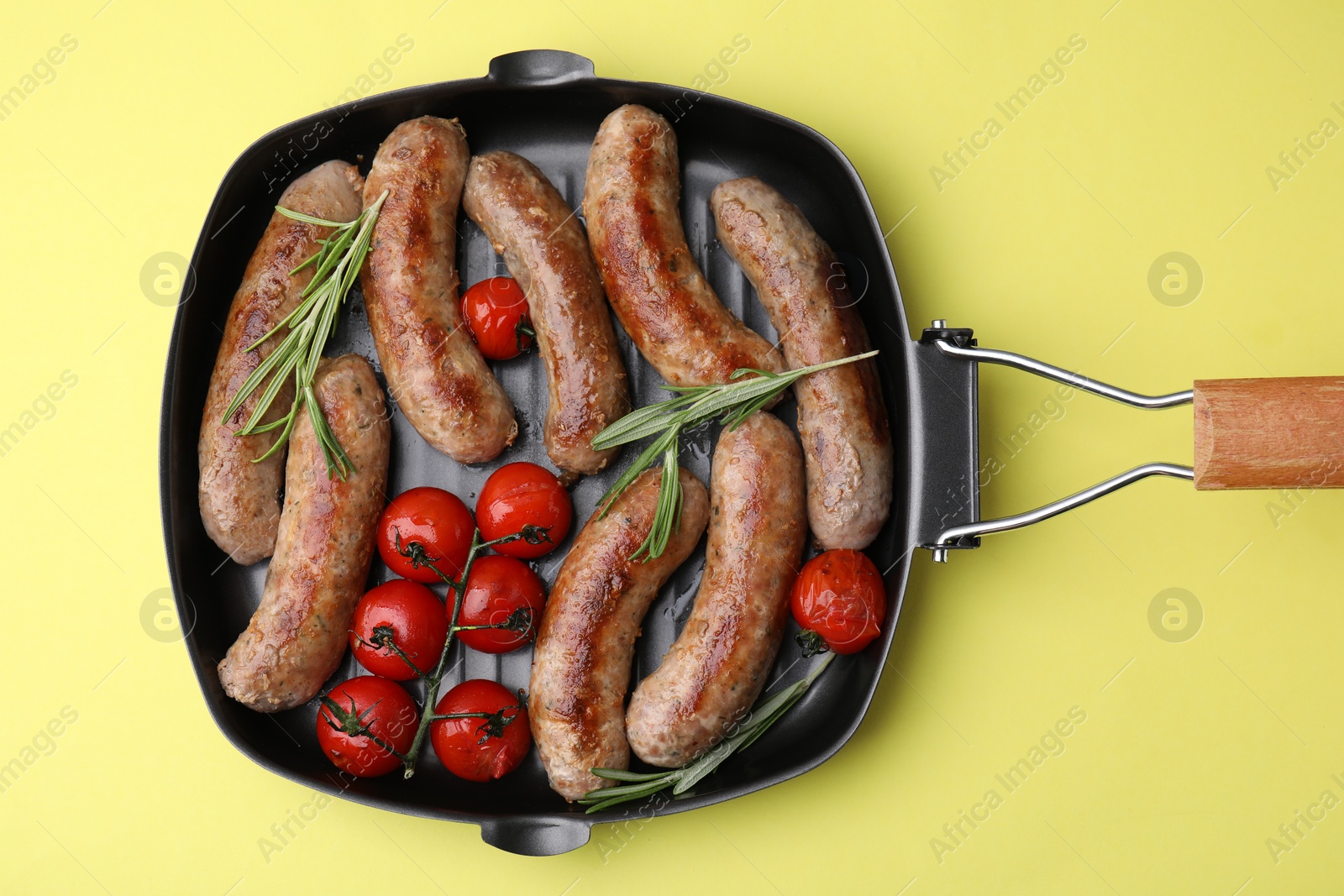 Photo of Grill pan with tasty homemade sausages, rosemary and tomatoes on yellow table, top view