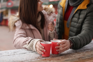 Photo of Young couple with cups of mulled wine at winter fair, closeup