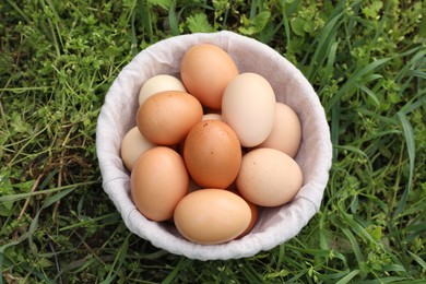 Photo of Fresh chicken eggs in basket on green grass outdoors, top view