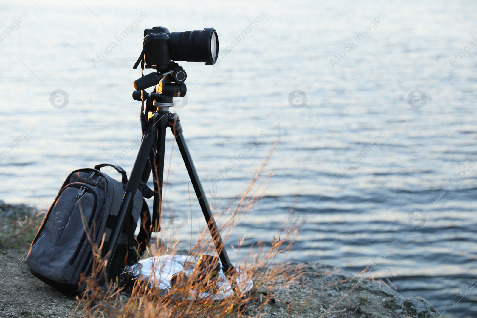 Photo of Tripod with modern camera and set of photography equipment on rocky river coast. Space for text