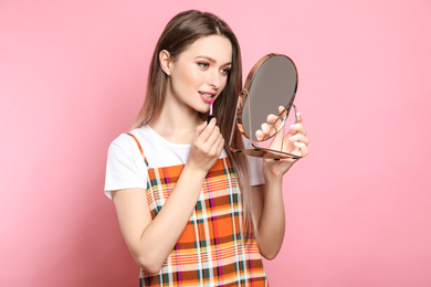 Photo of Beauty blogger applying lipgloss on pink background