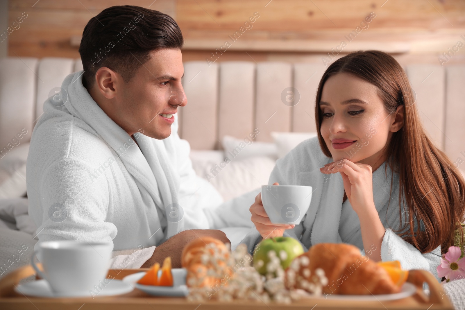 Photo of Happy couple in bathrobes having breakfast on bed at home