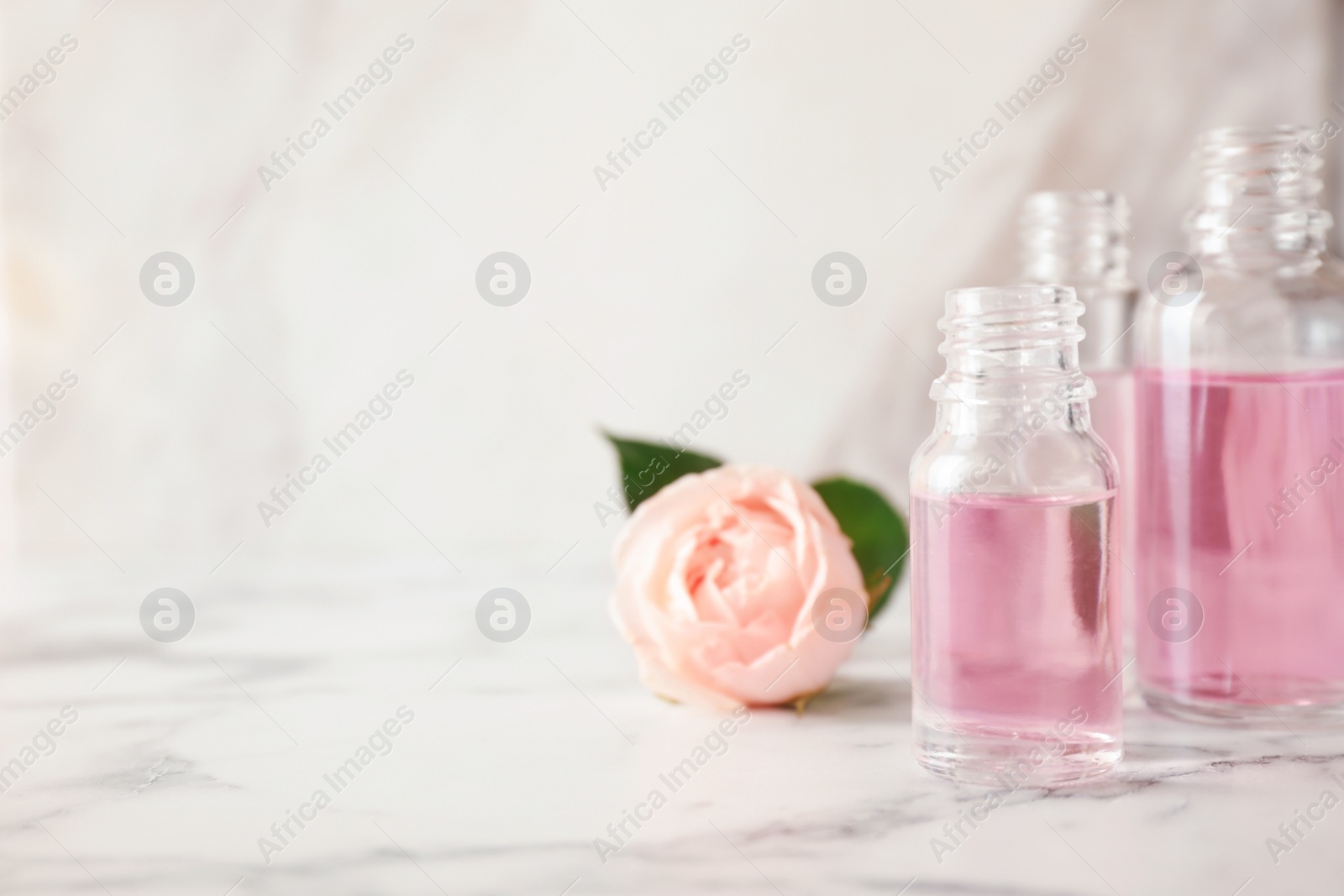 Photo of Bottles of essential oil and rose on marble table. Space for text